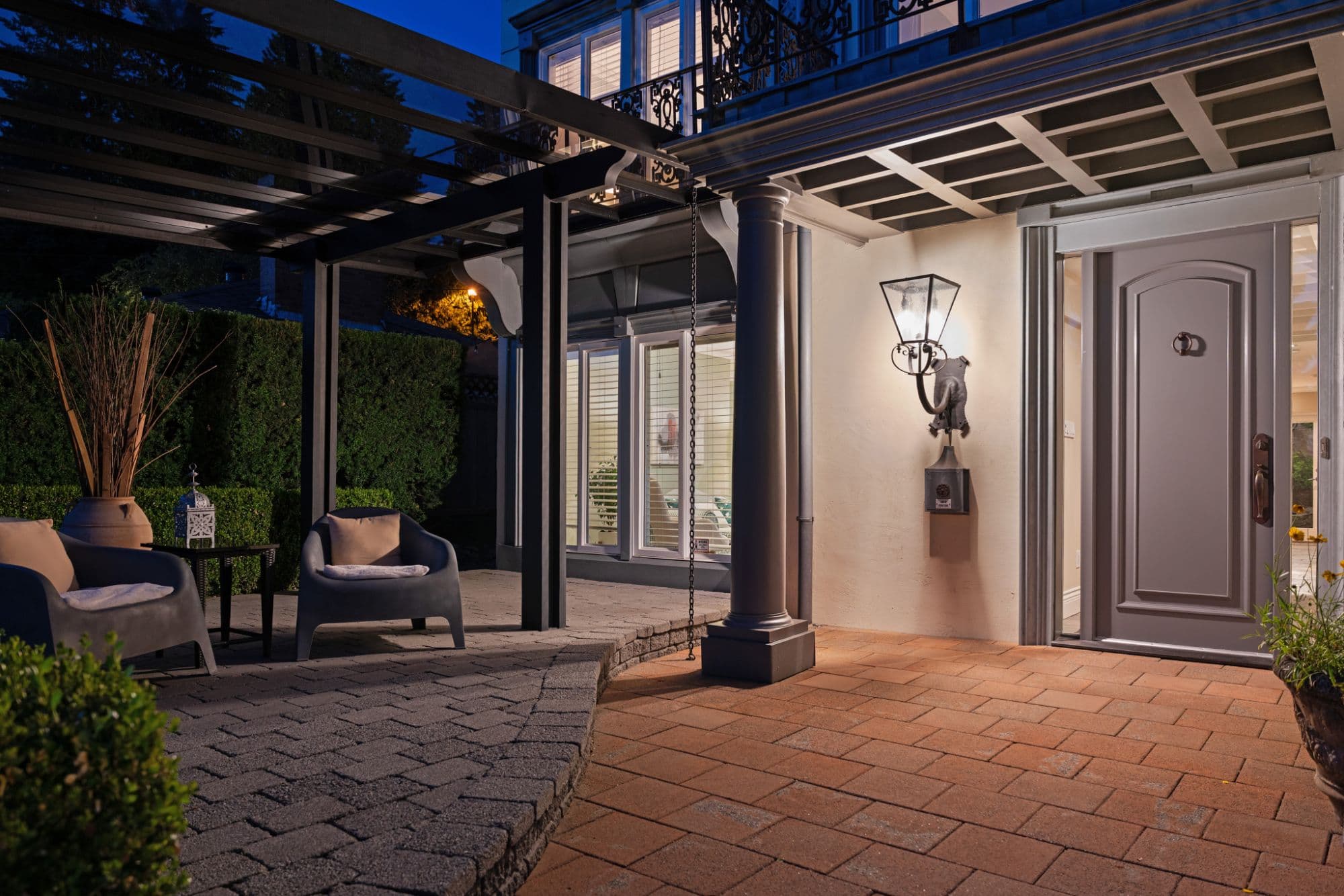 Front entrance and covered patio of a home at dusk, with a pergola, lantern and grey panelled door
